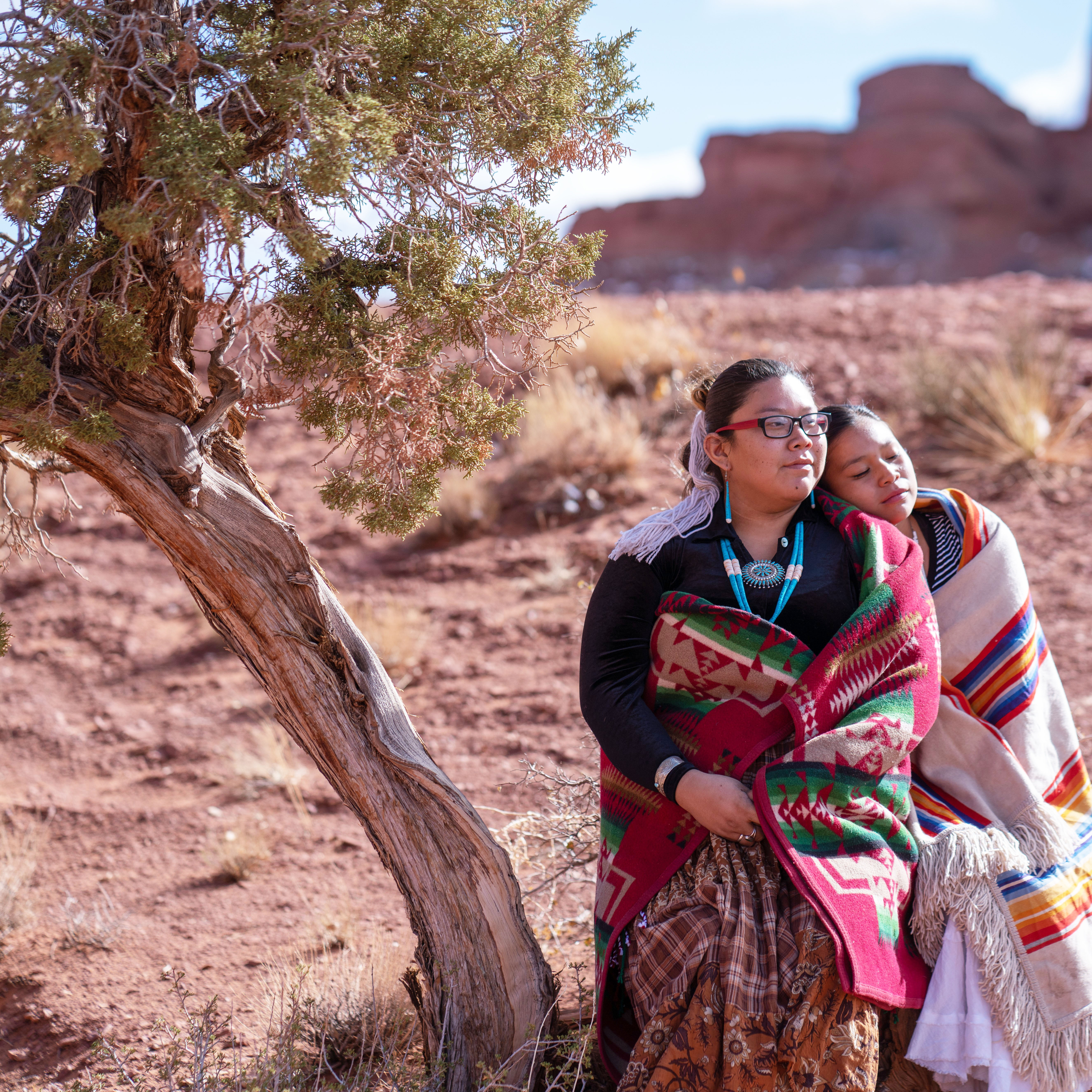 Two young Women wrapped in woven blankets sitting next to a tree