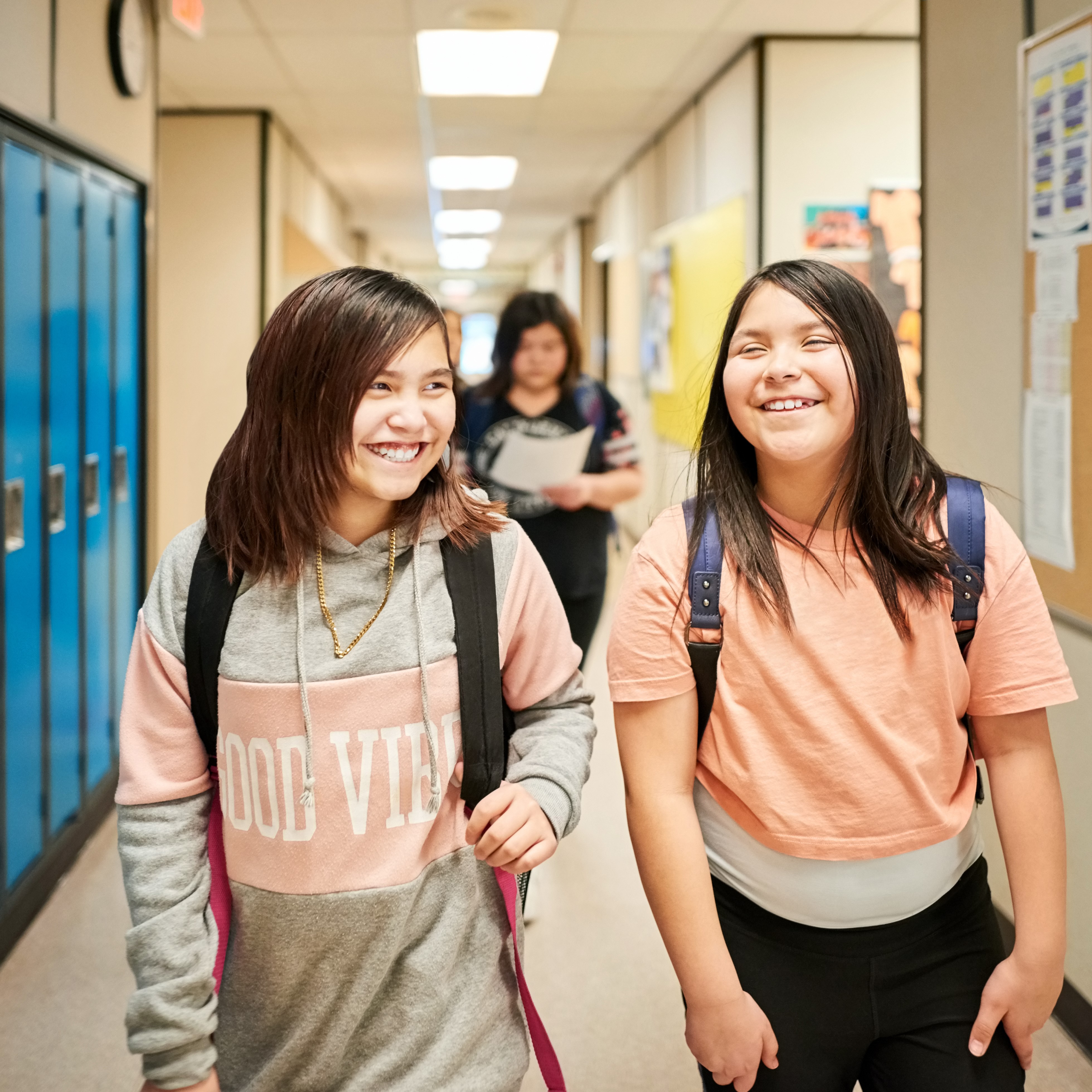 Two middle school kids walking down  a school hallway.